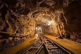 Historic Gold Bug Mine tunnel with narrow-gauge railway tracks leading deep into the illuminated underground shaft, where visitors can experience gold panning near the Bella Vista Bed and Breakfast Inn.